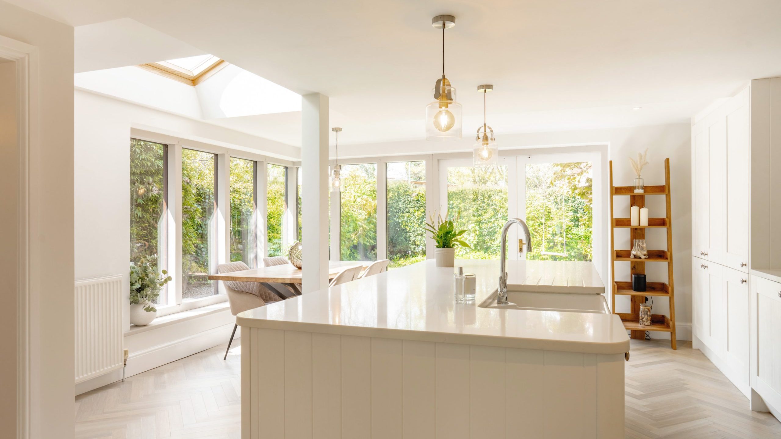 Bright and airy modern kitchen with a large island, white cabinets, and hardwood floors. the space features ample natural light from windows and a skylight, with a dining area visible in the background.