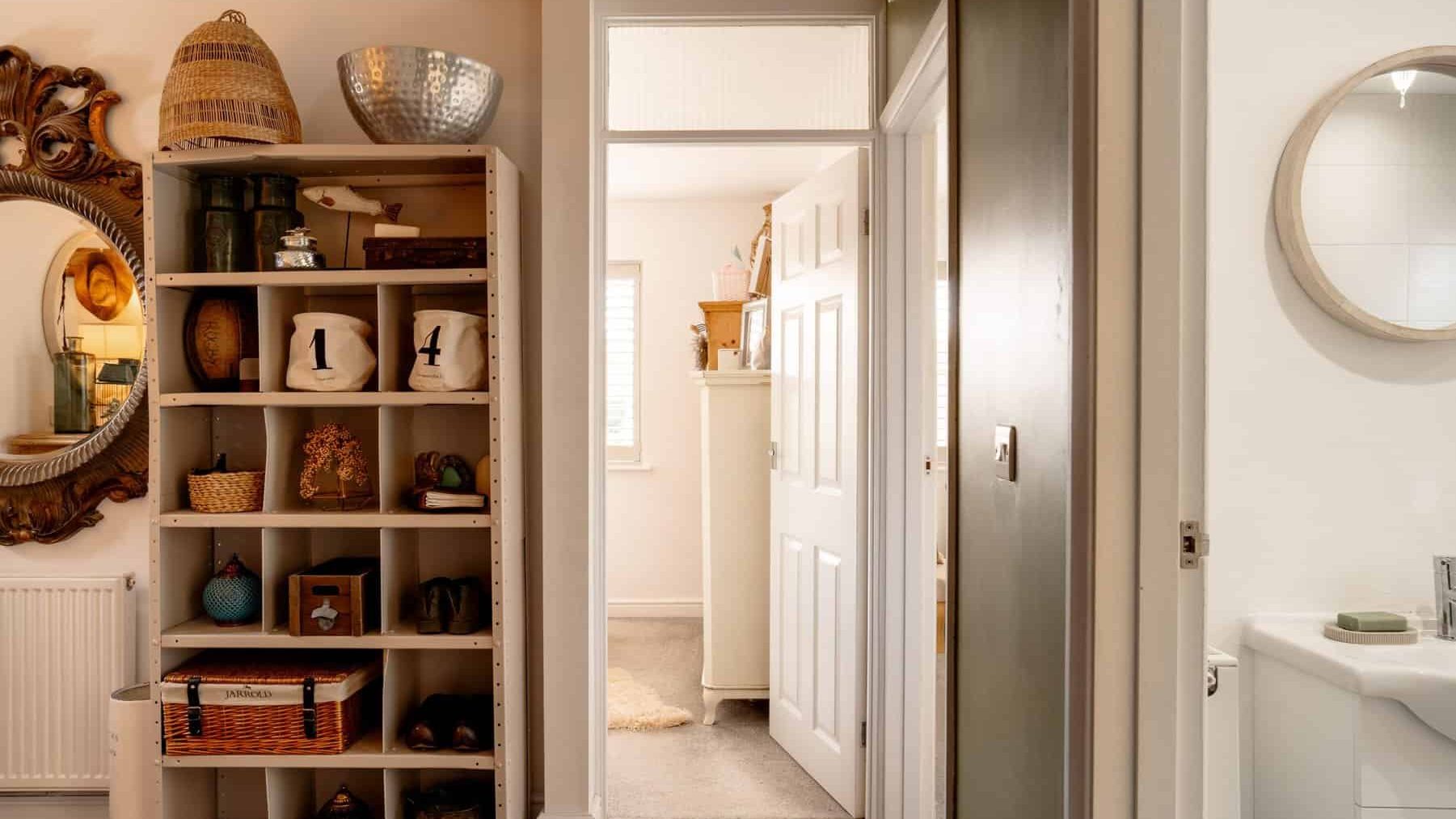 A cozy home interior featuring an open door leading to another room with a white shelf filled with decorative items on the left and a bathroom with a sink on the right.