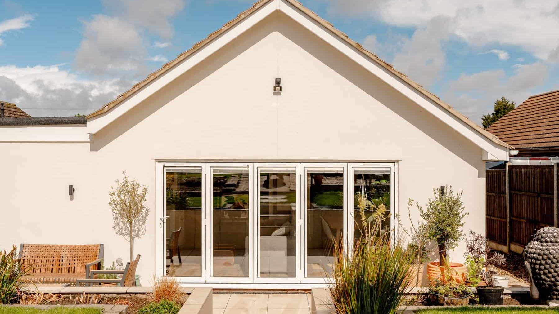 A well-maintained, modern, single-story home with a gabled roof, featuring large sliding glass doors and a straight garden path leading up to it. two small trees flank the entrance in a neatly landscaped yard.