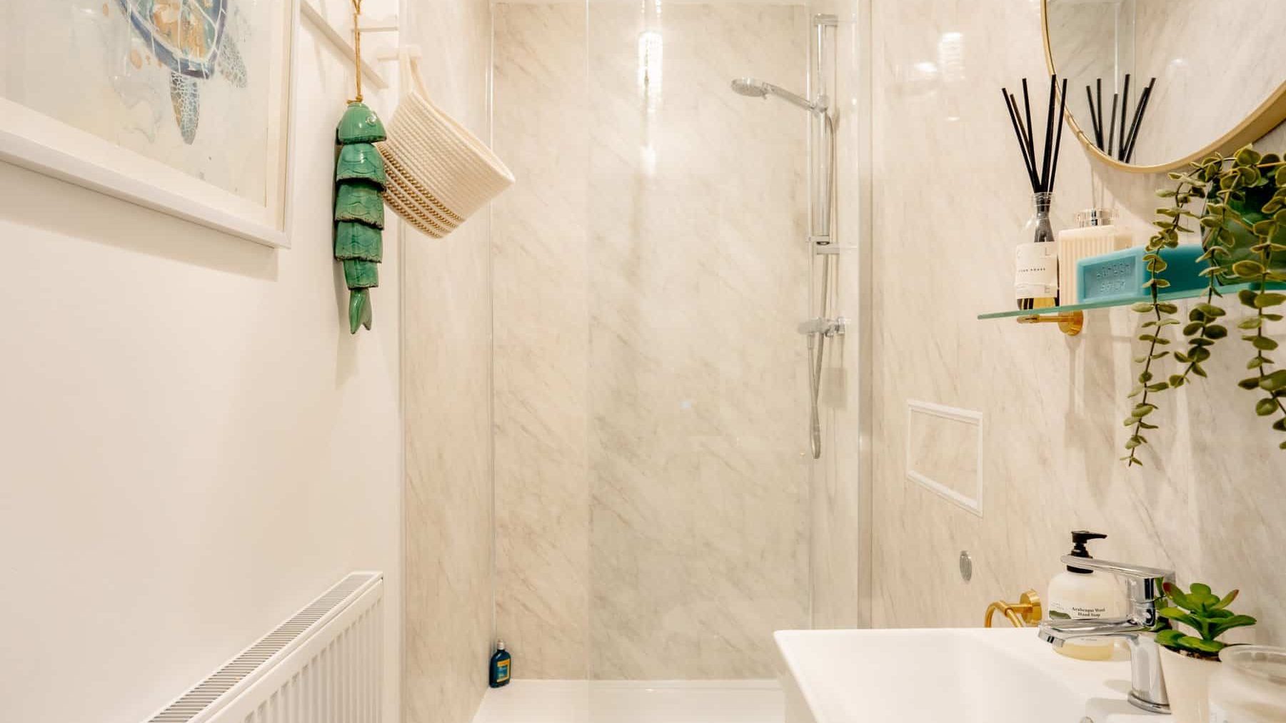 Modern bathroom with marble walls, featuring a walk-in shower, bathtub, and decorative plants. accessories include hanging green towels and wall-mounted shelving with toiletries.