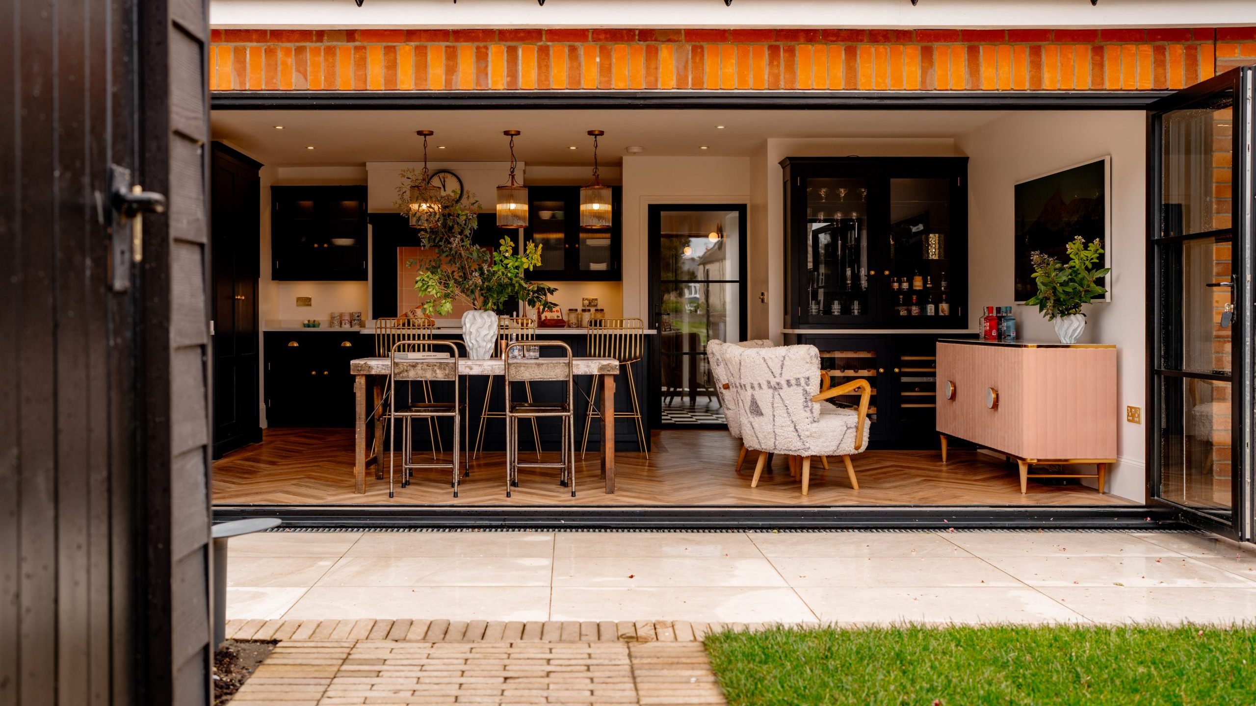 View through an open door leading to a stylish kitchen with an island and a dining area, featuring modern furniture and warm lighting. the setting emphasizes indoor-outdoor living.