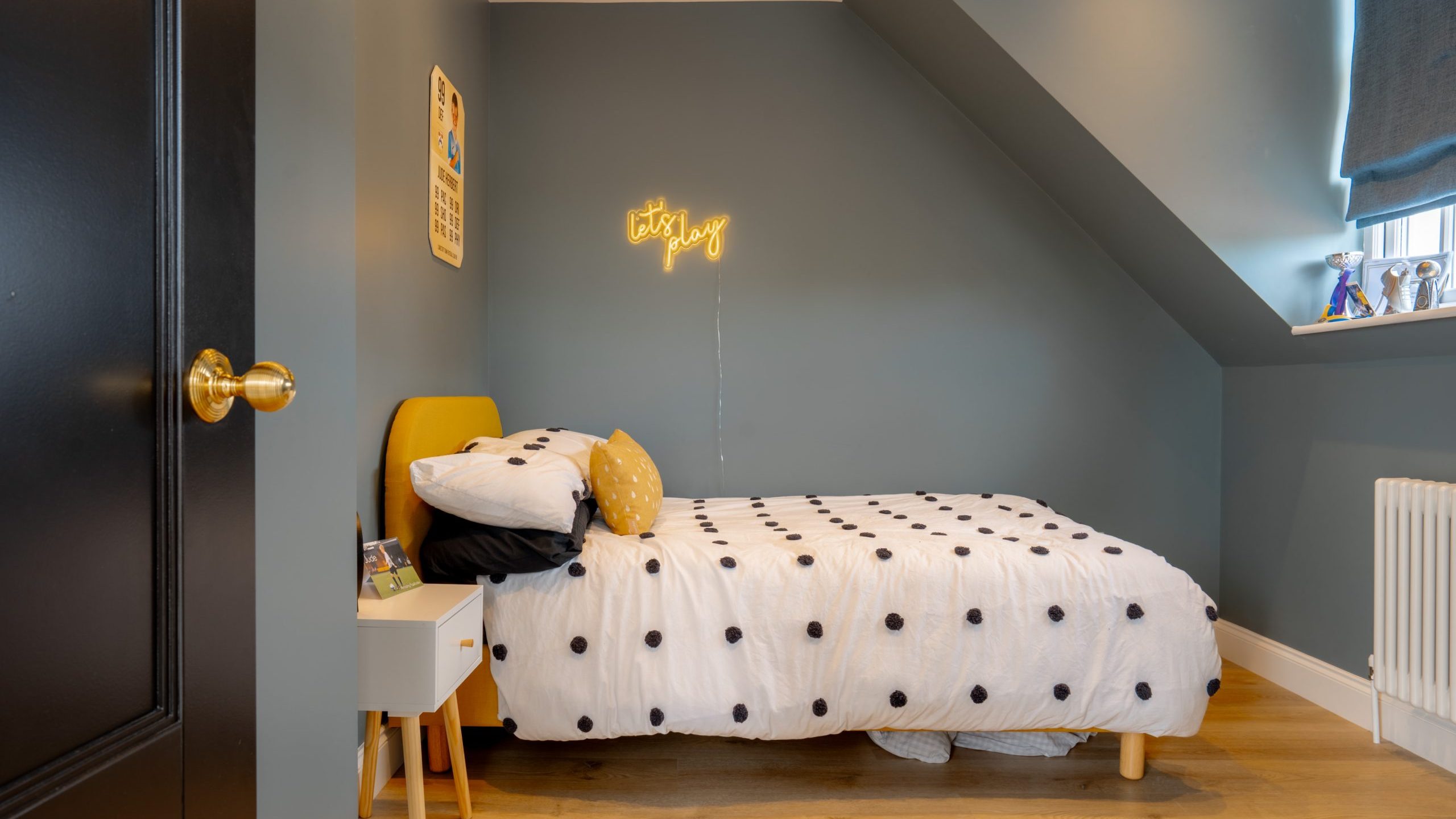 A cozy, modern child's bedroom featuring a single bed with a polka dot comforter and a large panda head pillow. a neon sign saying