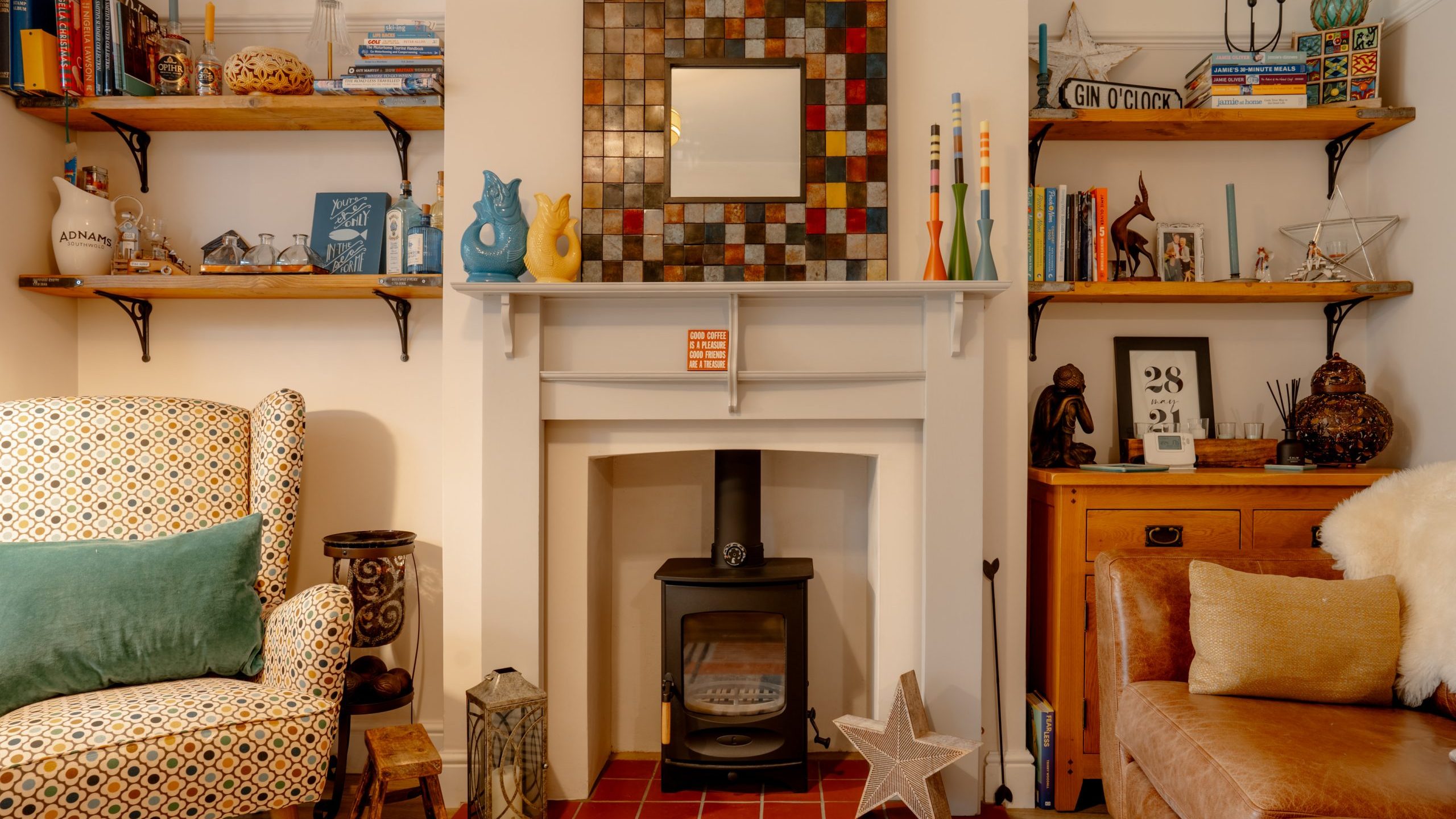 Cozy living room corner featuring a wood stove, vibrant sofa, patterned armchair, and shelves decorated with books, art, and various trinkets.
