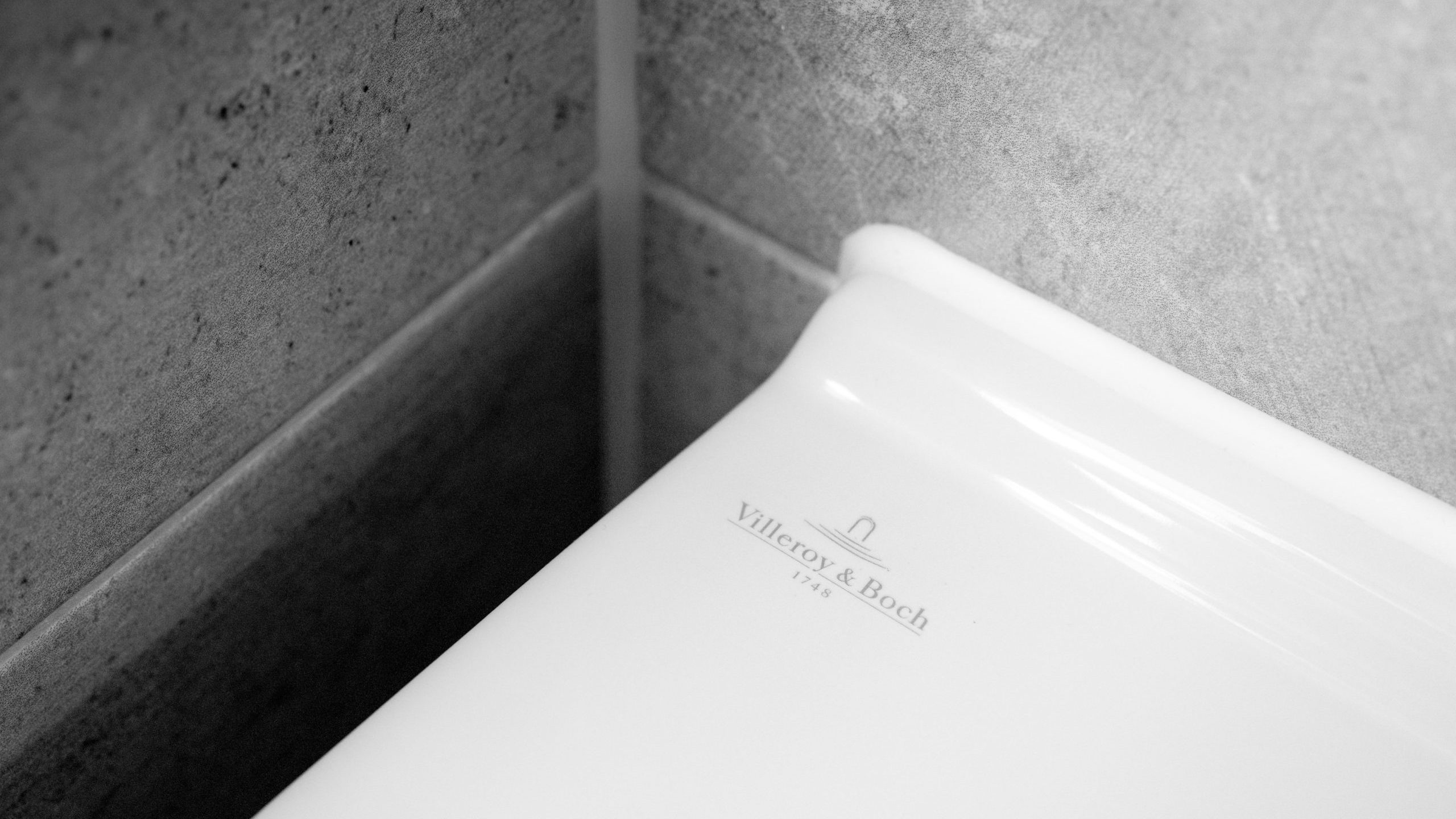 Close-up of a white Villeroy & Boch toilet positioned against a gray tiled wall corner. The brand name and logo are visible on the toilet in subtle gray lettering.