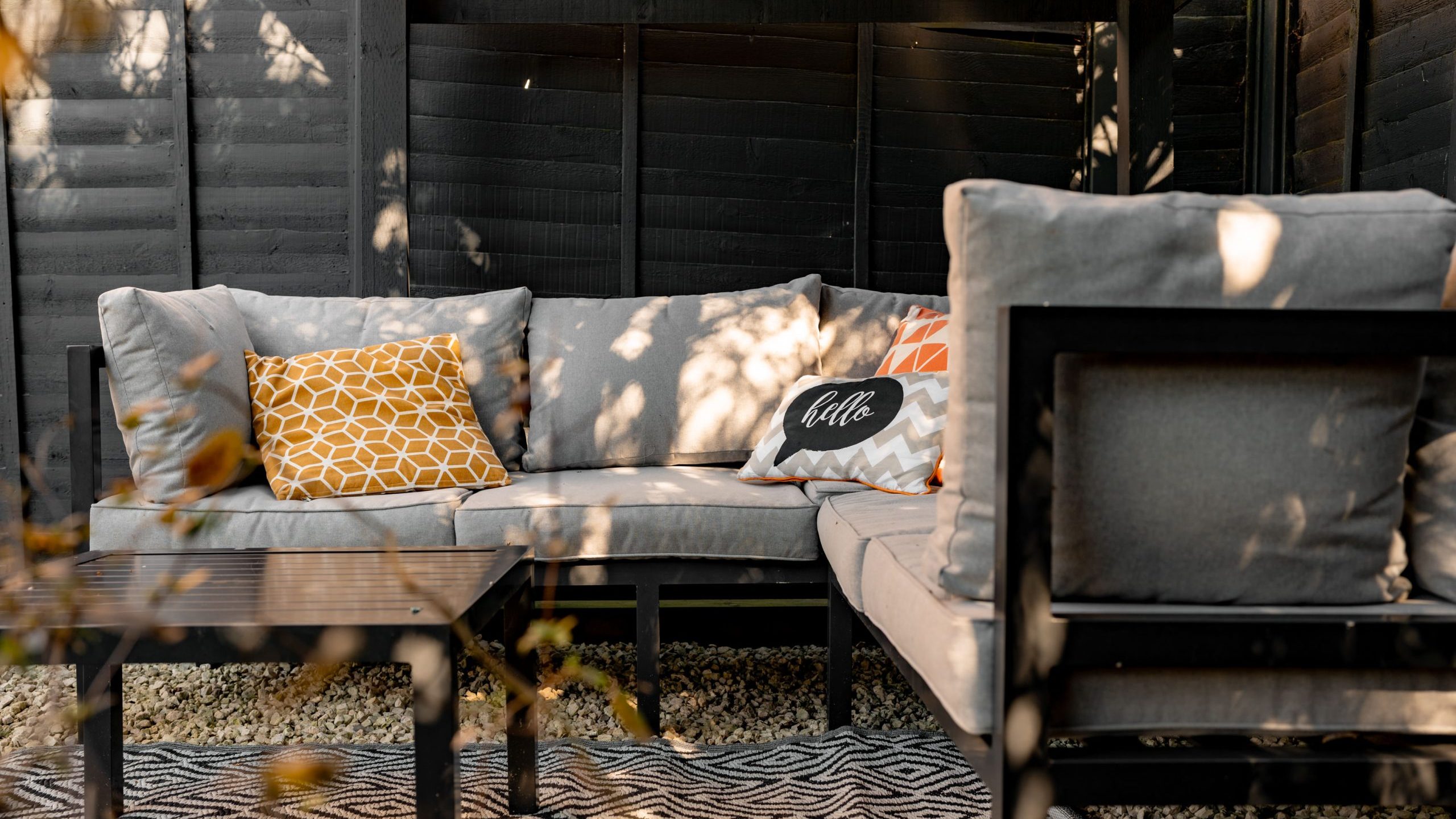 Outdoor seating area with black cushions and decorative pillows, including one with the word