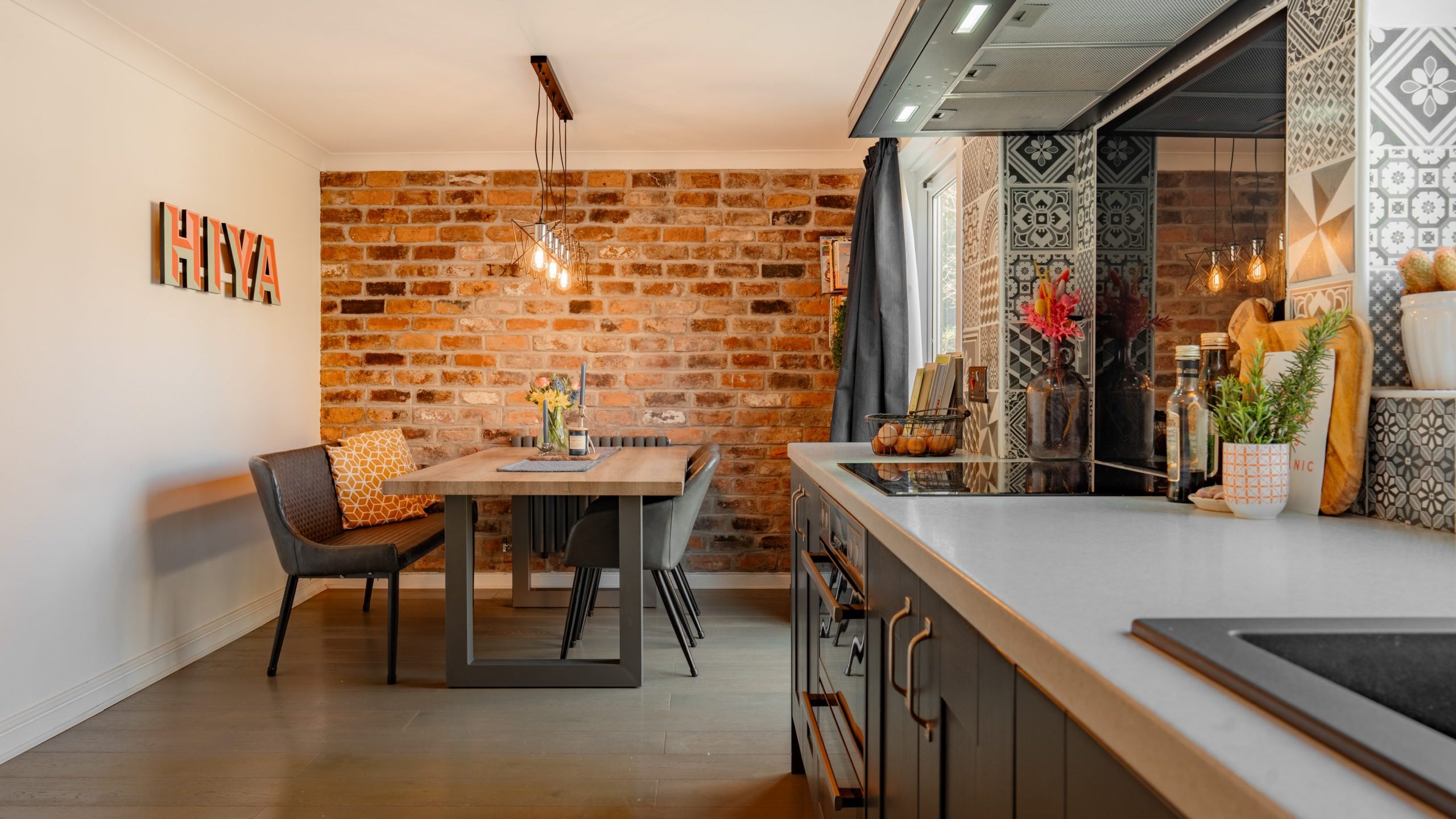 A modern kitchen and dining area featuring a brick accent wall with wall art spelling