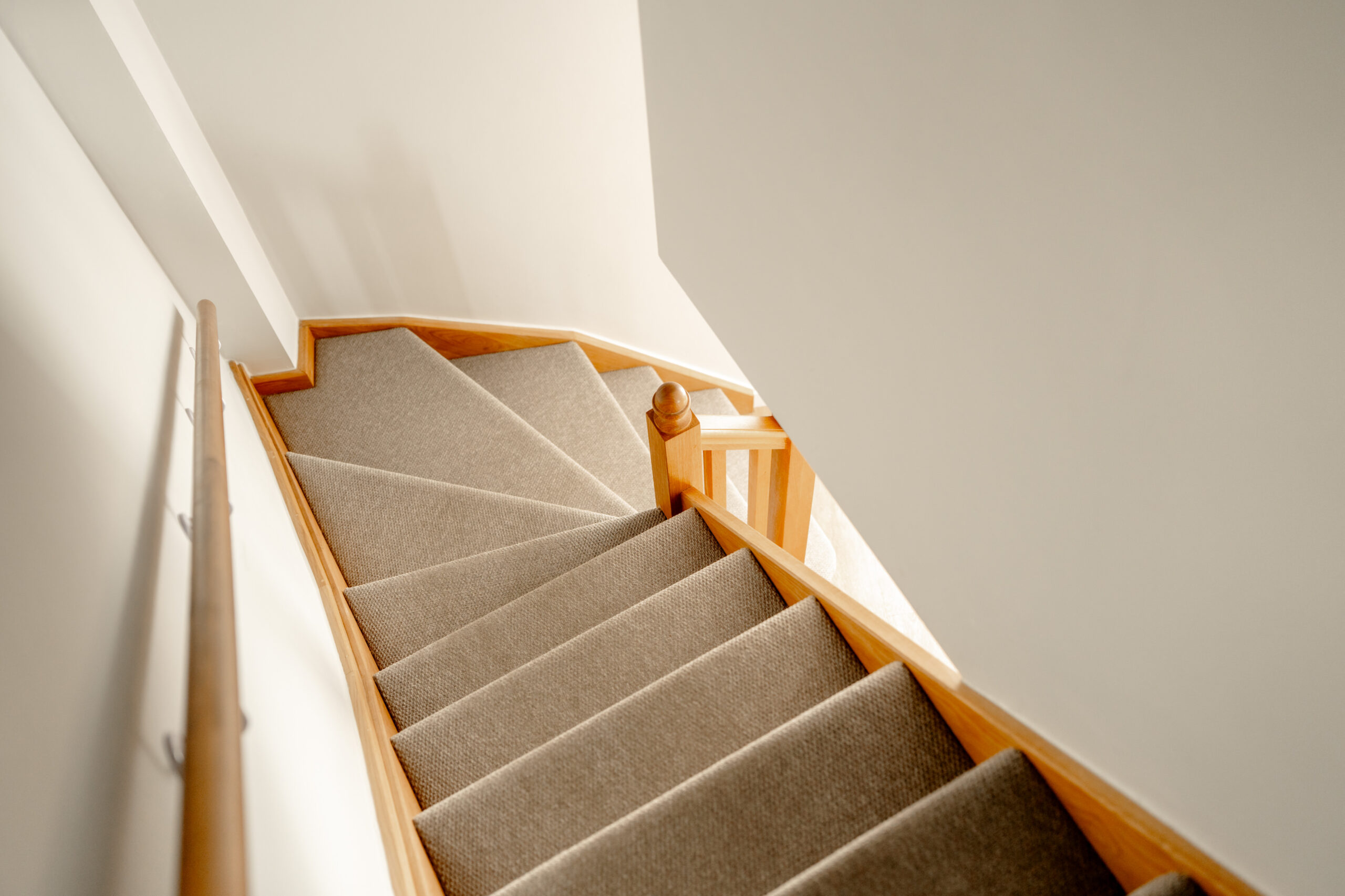 A carpeted staircase with wooden banisters curves downward against white walls, viewed from above.